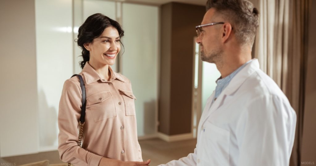 Female patient shaking hands with a plastic surgeon during a consultation (model)