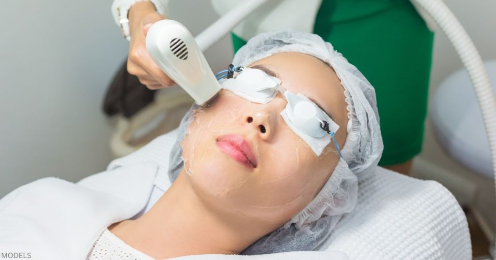 Woman receiving laser skin rejuvenation treatment from a provider using a handheld device (MODELS)