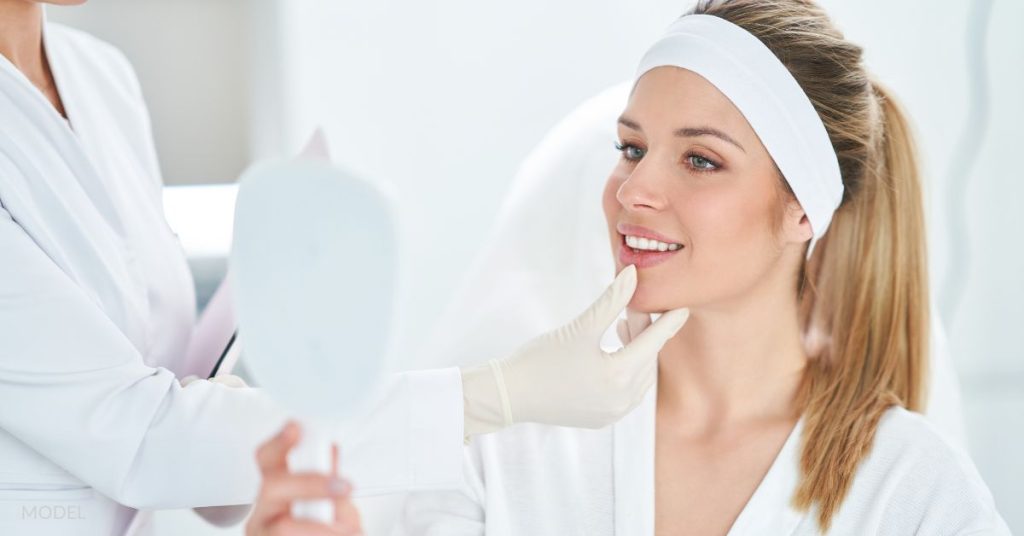 In a treatment room, a happy woman holds a mirror, reviewing BOTOX results with her injector. (models)